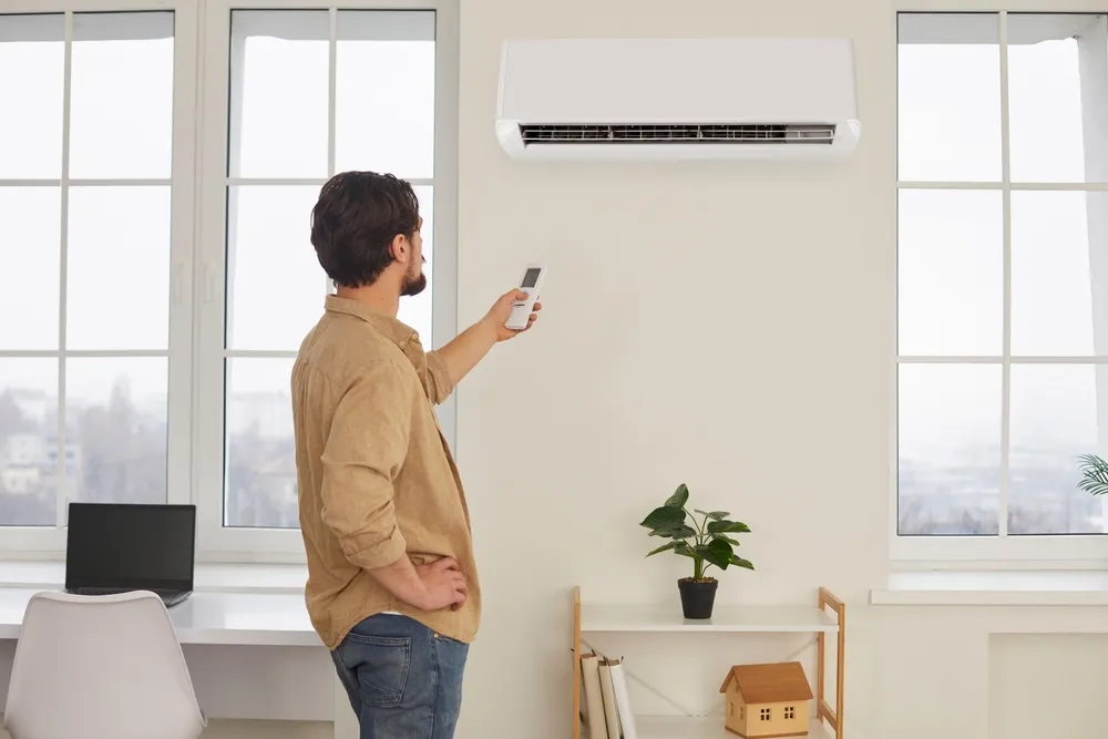 Homme réglant une climatisation murale avec sa télécommande.